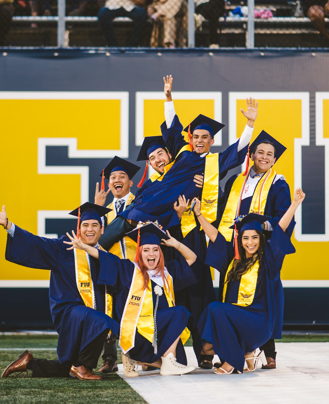FIU Students smiling with their diplomas on a football field after graduation